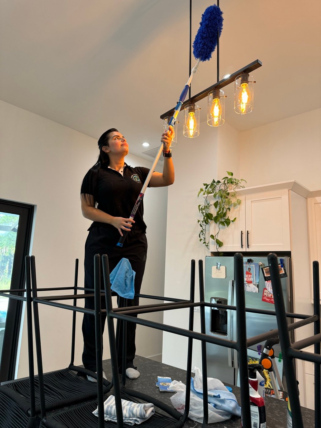 Angely dusting a kitchen light fixture with an extension duster